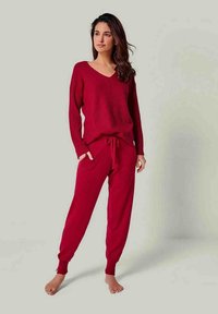 Rotes Strick-Loungewear-Set mit einem V-Ausschnitt und langärmligem Oberteil sowie einer Hose mit Kordelzug und gerippten Bündchen, aus einem weichen strukturierten Stoff.