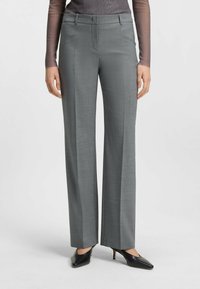 Grau maßgeschneiderte Hose mit glatter Textur, flacher Front und seitlichen Taschen. Kombiniert mit schwarzen High-Heels für einen formellen Look.