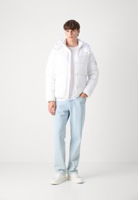 Vit puffjacka med huva, med dragkedja och framfickor. Kombinerad med ljusblå jeans och vita sneakers.