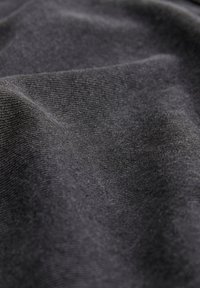 Tessuto nero con una trama fine, che mostra onde morbide e ondulate e sottili variazioni di tonalità. La superficie appare liscia e leggermente elasticizzata.