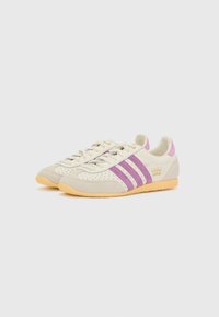 Gräddfärgade och lila sneakers med tre ränder, i mockamaterial, med perforerade detaljer på ovandelen och en gummisula. Anmärkningsvärd branding på sidan.