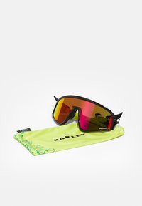 Óculos de sol com armação preta e lentes espelhadas vermelhas, acompanhados por um saco macio verde com o nome da marca "Oakley."