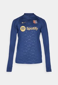 Marineblauw longsleeve tricot met halflange ritssluiting, voorzien van een gestructureerd ontwerp, Nike-logo, FC Barcelona-embleem en gouden Spotify-embleem op de borst.