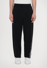 Black sweatpants with an elastic waistband and a loose fit. Notable detail includes white text printed along the left leg.