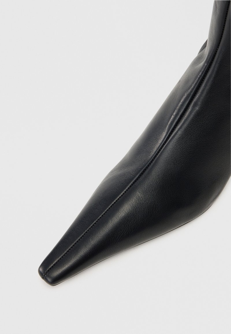 Svart läderankelboots med spetsig tå och slät yta. Har en elegant design och sömmar längs sidan.