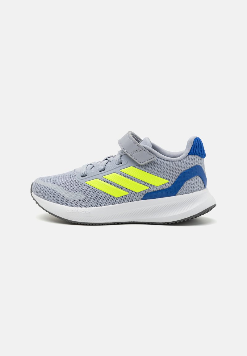 Botte de sport grise avec une tige en maille, présentant des rayures jaunes vives, un accent de talon bleu et une fermeture à bande auto-agrippante.