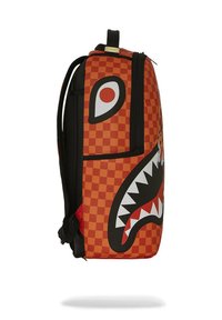 Mochila a cuadros naranja con un diseño de cara de tiburón que incluye dientes, acentos negros y un asa en la parte superior. Fabricada con material texturizado y duradero.