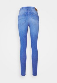 Vaqueros de denim ajustados en azul claro con un lavado desgastado, que presentan dos bolsillos traseros y una etiqueta de cuero marrón en la cintura.