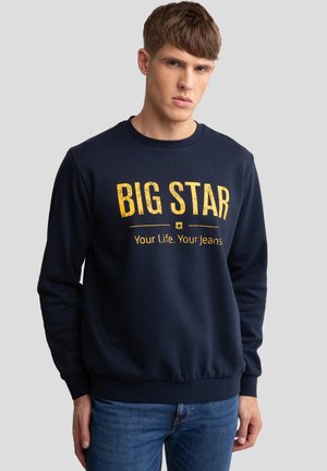 Navy blauwe sweatshirt van een zachte stof heeft een ronde halslijn, lange mouwen en een opvallende gele opdruk met de tekst "BIG STAR."