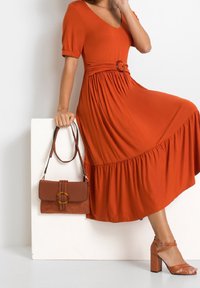 Rustowa midi sukienka z bufkami i marszczoną talią, z okrągłą klamrą. Dodatki to brązowa torebka i sandały na obcasie.