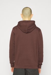 Sudadera marrón hecha de tejido suave, con una capucha grande, mangas largas y un corte relajado. Textura suave con un diseño limpio y minimalista.