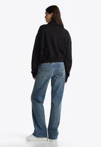 Zwarte cropped sweatshirt met een ribbelrand en verlaagde schouders, gecombineerd met hoge taille blauwe jeans met achterzakken en een relaxte pasvorm.
