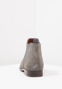 Bottes chelsea en daim gris avec panneaux latéraux élastiques, bout arrondi et petit talon en bois marron. Des coutures décoratives rehaussent le design.