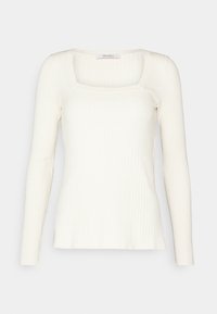 Kermakrokanen ribbatunika pitkällä hihalla ja neliömäisellä kaula-aukolla, tiukka siluetti ja Max Mara -lähetys kauluksessa.