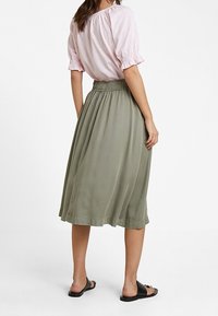 Khaki midi-hame, jossa on joustava vyötärö, sileä pinta ja lentävä laskos, yhdistettynä vaaleanpunaiseen raidalliseen lyhythihaiseen paitaan.