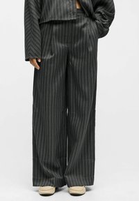 Pantalons à rayures noires et blanches, larges et à jambe large en tissu léger et lisse. Présentent une taille haute avec une coupe décontractée et un léger éclat.