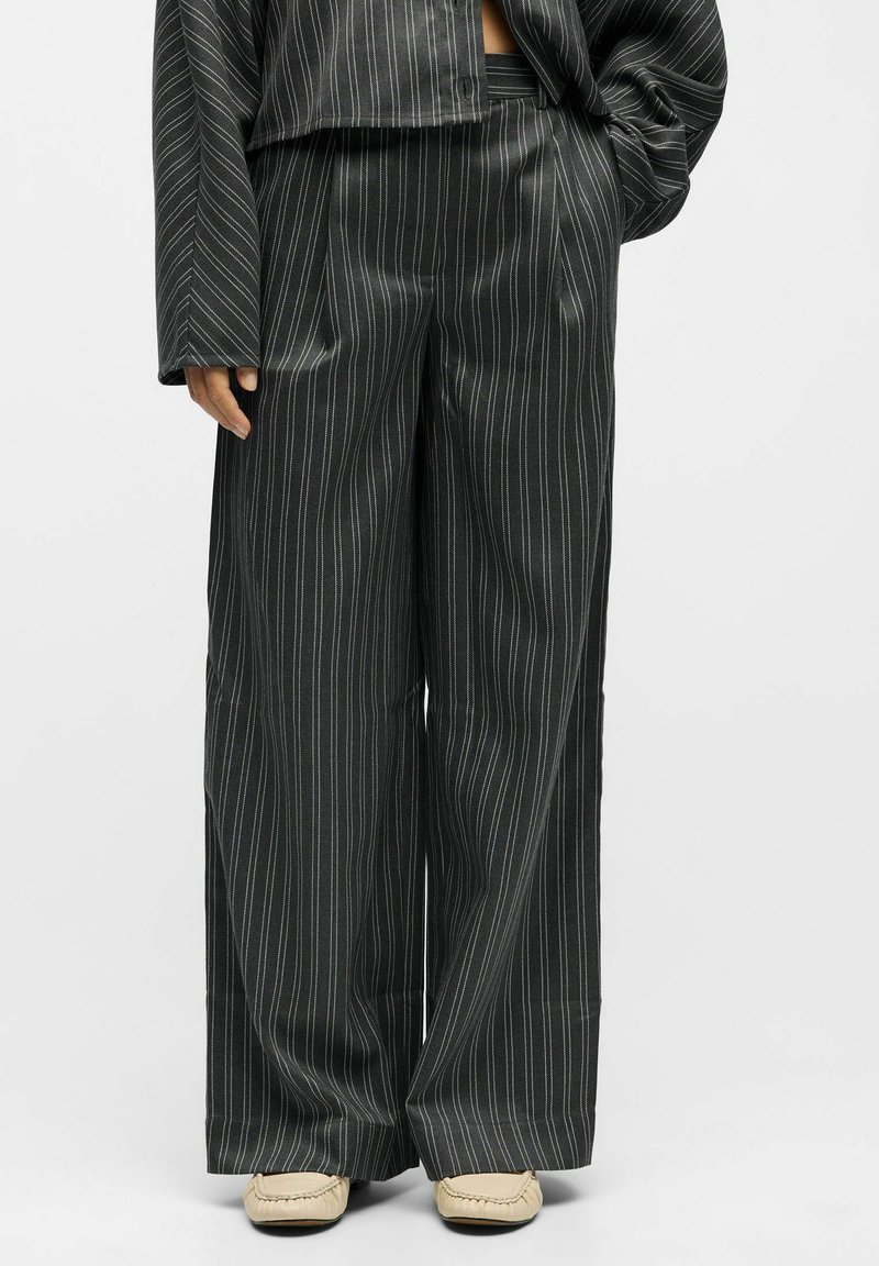 Pantalons à rayures noires et blanches, larges et à jambe large en tissu léger et lisse. Présentent une taille haute avec une coupe décontractée et un léger éclat.