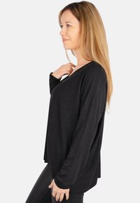 Schwarzes Langarmoberteil mit V-Ausschnitt, aus einem weichen Material gefertigt, mit lockerer Passform und seitlichen Schlitzen für mehr Bewegungsfreiheit.