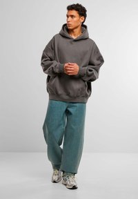 Overdimensjonert grå hettegenser med kengurulomme og ribbestrikkede mansjetter, kombinert med løse, lyseblå denimbukser og metalliske joggesko.