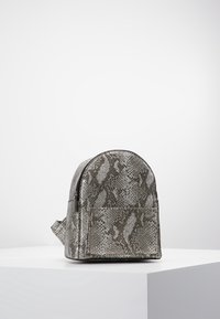 Mochila con estampado de serpiente gris, de forma redondeada, con cierre de cremallera y un bolsillo frontal. Material texturizado con un brillo sutil.