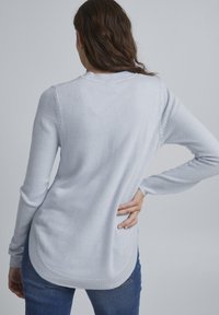 Lyseblå sweater med lange ærmer, rund halsudskæring og en buet kant. Stoffet ser blødt ud med en subtil tekstur.