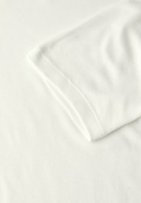 Valkoinen puuvillapaita, jossa on lyhyet hihat ja sileä rakenne, näkyvillä saumoilla ja siistillä, minimalistisella muotoilulla.