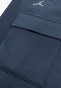 Υφασμα μπλουζας σε ναυτικό μπλε χρώμα με επίπεδη τσέπη και ανάγλυφο λευκό λογότυπο Jumpman. Ορατή είναι η λεία υφή και οι τακτικές ραφές.