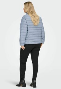 Světle modrá prošívaná bunda s vodorovným prošíváním, vysokým límcem a zkráceným střihem, doplněná černými úzkými džíny a kotníkovými botami.
