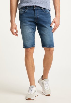 Shorts de mezclilla en lavado azul claro, con un dobladillo desgastado y lazos para cinturón. Combinados con zapatillas deportivas en gris y blanco, que destacan por su diseño deportivo.