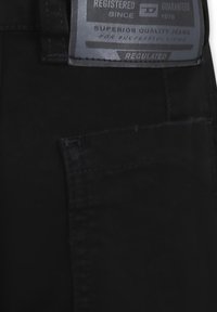 Jeans in denim nero con una tasca posteriore visibile e un'etichetta di marca, caratterizzati da una finitura opaca e cuciture a contrasto per un tocco di dettaglio in più.