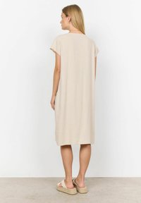 Beiges, knielanges Kleid mit kurzen Ärmeln und lockerer Passform. Weicher Stoff mit glatter Textur. Getragen mit Espadrilles.