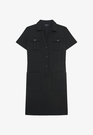 Mustapaita, joka on valmistettu pehmeästä kankaasta ja jossa on napitus edessä, lyhyet hihat, kaksi rintataskua ja kaksi suurta sivutaskua.