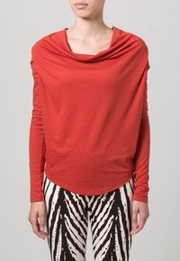 Czerwona bluzka z długim rękawem i drapowanym dekoltem, połączona z legginsami w czarno-białe paski z odważnym abstrakcyjnym wzorem.