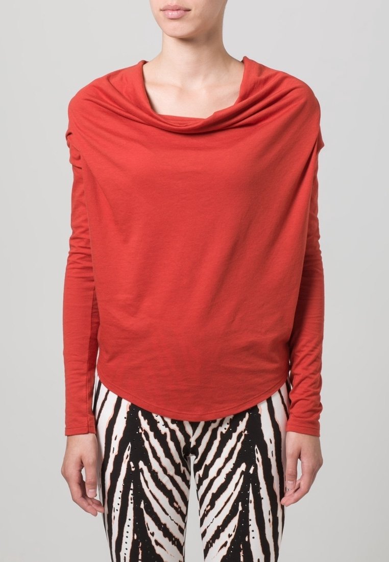 Czerwona bluzka z długim rękawem i drapowanym dekoltem, połączona z legginsami w czarno-białe paski z odważnym abstrakcyjnym wzorem.