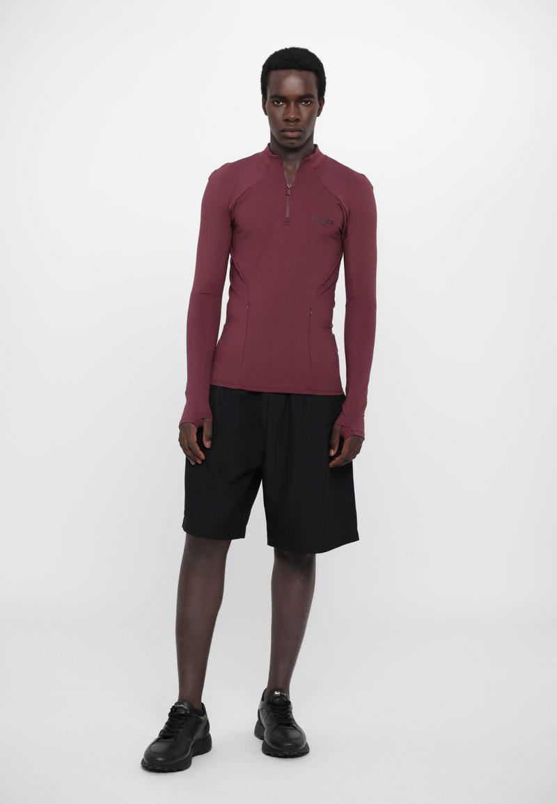Maroon long-sleeve top with a zippered neckline, paired with black shorts. The outfit features a sleek, fitted design with smooth texture.