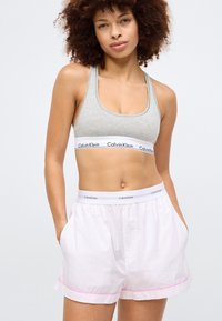 Grå bomulls sports-bh med en hvit Calvin Klein-logo-bånd; rosa og hvite stripete vevde shorts med sidelommer og matchende midjebånd.