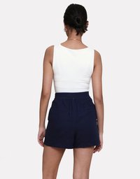 Weißes ärmelloses Oberteil mit rundem Ausschnitt, kombiniert mit marineblauen Shorts mit elastischem Bund und zwei Gesäßtaschen.