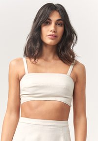 Hele beež linasest cropped top õhukeste rihmadega, sirge dekoltee ja liibuv disain, koos sobiva kõrge vöökohaga seelikuga.