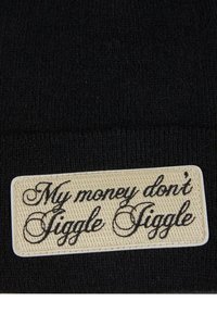 Svart strikket lue med en rektangulær beigefarget lap sydd på, med teksten "My money don't Jiggle Jiggle" i svart kursiv.