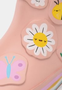Superficie rosa con adesivi colorati a tema cartone animato, tra cui una margherita sorridente, farfalle e forme di api.
