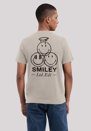 Helle graue T-Shirt mit drei schwarzen Smileys, wobei einer Kopfhörer trägt und ein anderer einen Heiligenschein hat, beschriftet mit "SMILEY Ltd. Edt 1972."