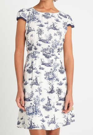 Vit klänning med marinblå toiletryck som visar pastorala scener, rundad halsringning, korta rynkade ärmar och en figurnära midja med utsvängd kjol.