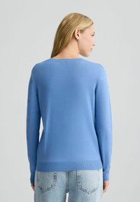 Hellblaue gestrickte Sweater mit langen Ärmeln, die subtile kreisförmige Muster entlang der Ärmel, einen gerippten Saum und einen runden Ausschnitt aufweisen.