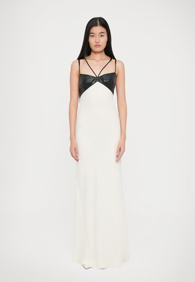 Robe maxi en tissu texturé blanc, avec un corsage en cuir noir et des bretelles fines, design triangulaire au niveau de la poitrine.