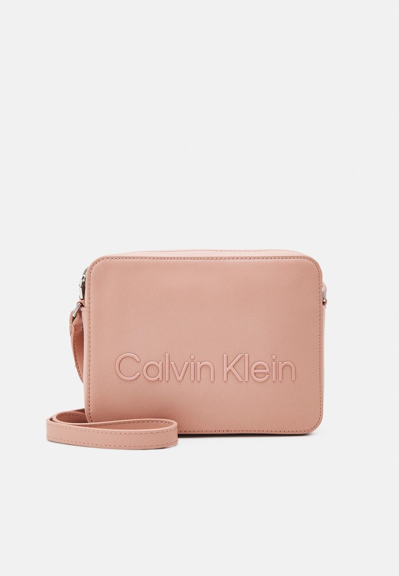Jasnoróżowa torebka na ramię z gładkiej skóry, z wytłoczonym logo "Calvin Klein", prostokątnym kształtem, regulowanym paskiem i zamknięciem na zamek.
