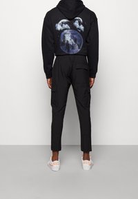 Svart hoodie med grafiskt tryck på baksidan, parat med svarta cargobyxor. Vita sneakers med orange detaljer. Strukturerad tyg.