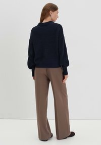 Maglione lavorato a maglia blu navy con colletto alto e vestibilità morbida, abbinato a pantaloni larghi color cammello, caratterizzati da una texture liscia e un design minimale.