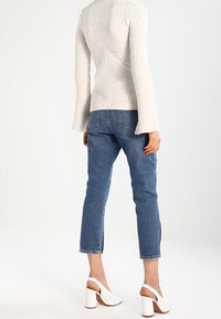 Lichtbeige geribde gebreide trui met uitlopende mouwen en diagonale naden, gecombineerd met halflange blauwe denim jeans met zijsplitten en witte blokhakken sandalen.