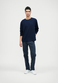 Tengerészeti hosszúujjú kerek nyakú póló, sötét farmernadrággal és fehér tornacipővel párosítva. Simas szövet, laza szabás és minimalista design.