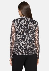 Przezroczysta bluzka z długim rękawem o falistym, czarno-kremowym abstrakcyjnym wzorze. Posiada okrągły dekolt i dopasowany fason, zestawiona z czarnymi spodniami.